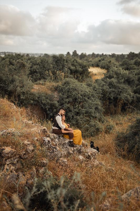 זוג יושב מחובק על סלע מעל נוף ירוק — צילומי זוגיות בטבע