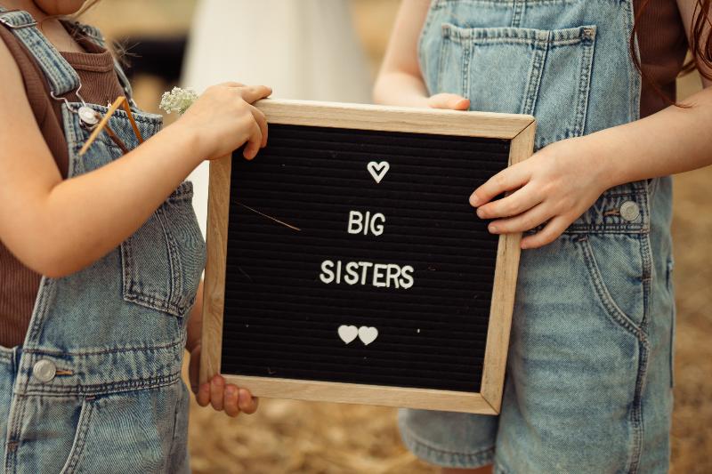 ידיים קטנות מחזיקות שלט BIG SISTERS – פרט מצילומי הריון עם ילדים