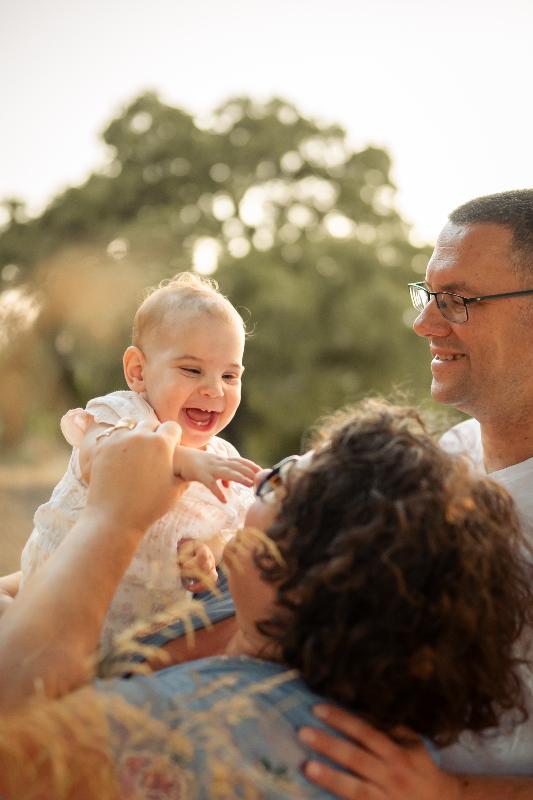 תינוקת צוחקת בידי ההורים באור רך – צילומי גיל שנה עם המשפחה
